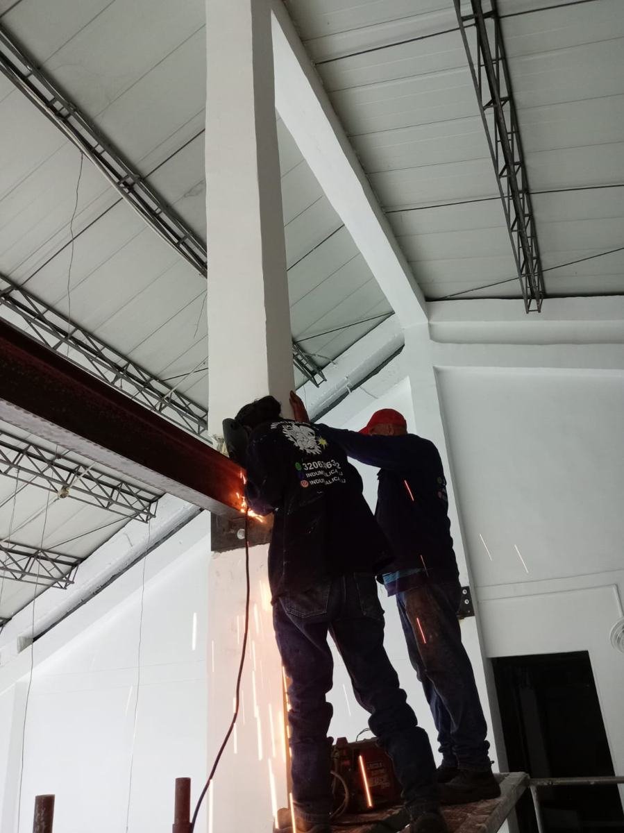 Dos soldadores montando una viga metálica sobre columna para mezzanine o estructura de techo